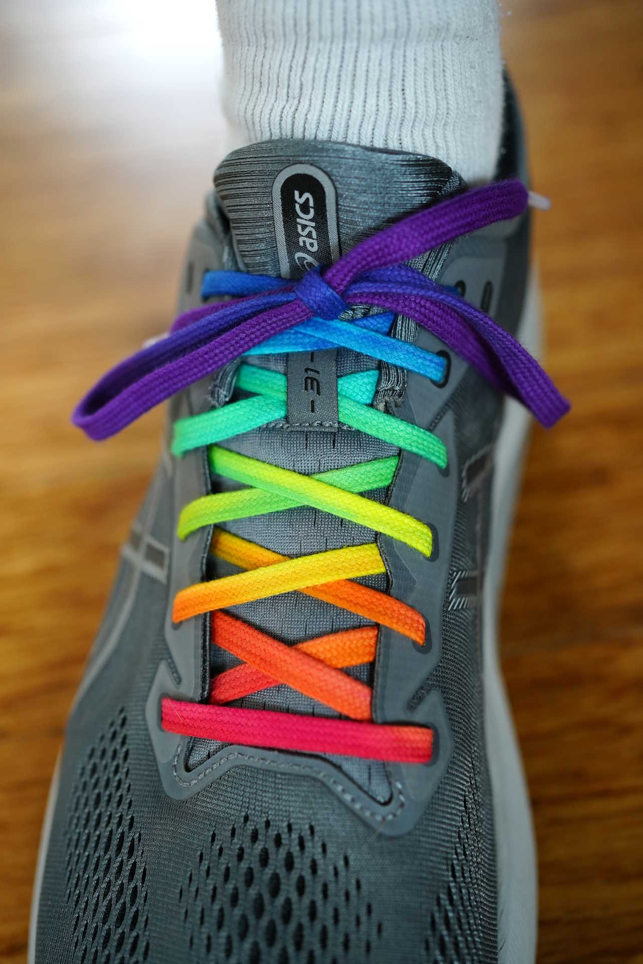 close up of shoe being worn on a foot, with rainbow laces tied
