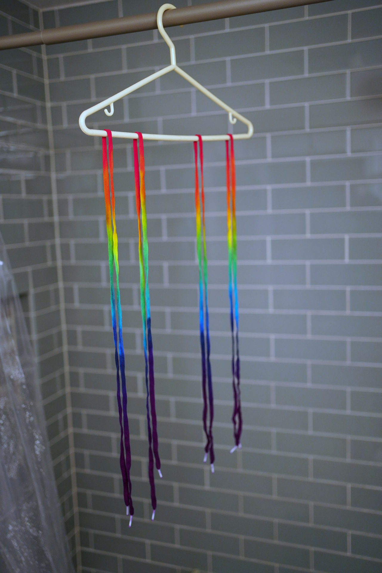 four rainbow-coloured shoelaces hanging from a hanger in the shower